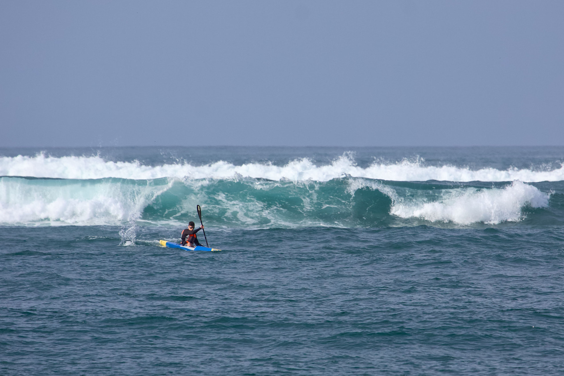 Palista remando frente a una gran ola en mar abierto